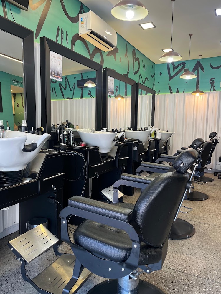 Salão da KFÉ Barbearia com cadeiras de barbeiro de couro preto, lavatórios brancos, espelhos e parede verde grafitada
