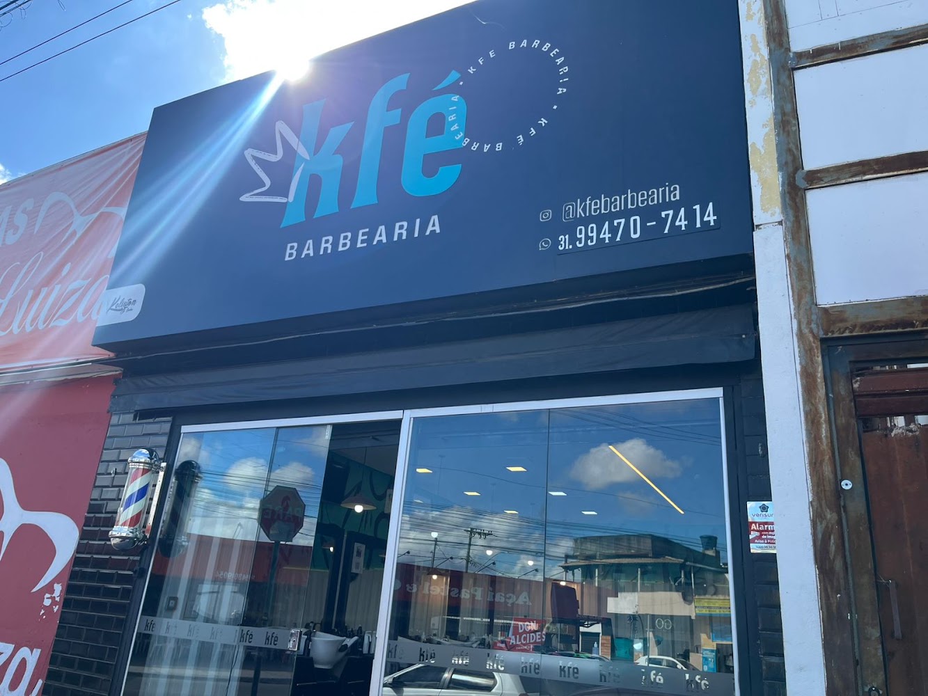 Fachada da KFÉ Barbearia com letreiro azul, poste de barbeiro na entrada e vitrine de vidro