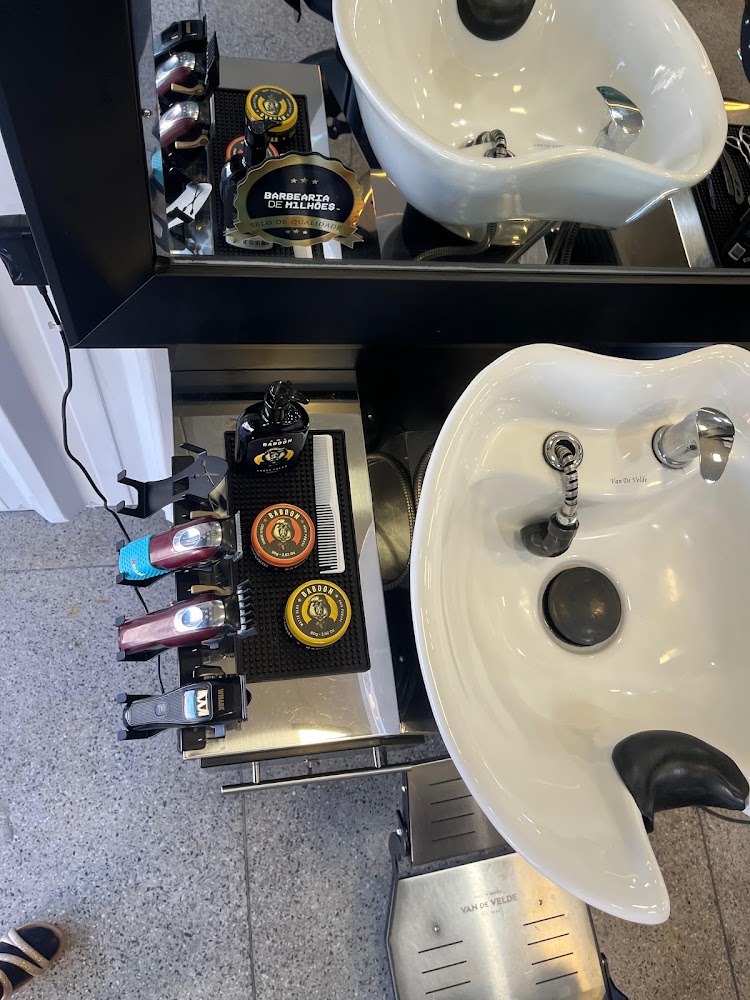 Bancada da barbearia com máquinas de corte, pente e pomadas ao lado dos lavatórios brancos